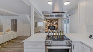 A modern kitchen with white cabinetry, a central island with a stove, and a stone backsplash. - Waterfront Cabin at White Pass, Mt. Rainier (Packwood)