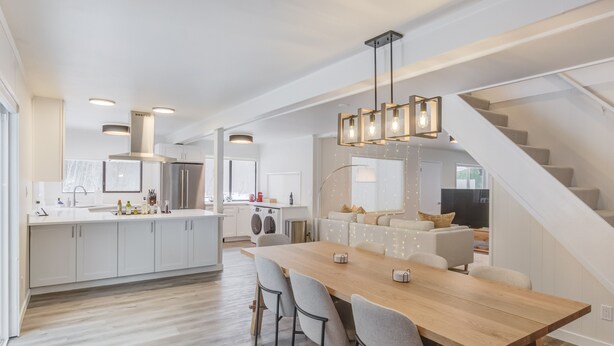 A modern kitchen with white cabinets, a wooden dining table, and a staircase leading to a loft area. - Waterfront Cabin at White Pass, Mt. Rainier (Packwood)