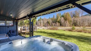 A hot tub under a covered patio with a view of a grassy area and trees. - Waterfront Cabin at White Pass, Mt. Rainier (Packwood)