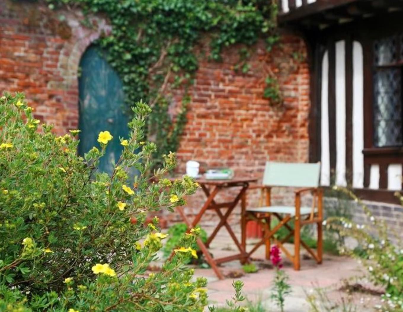Un espace extérieur aménagé dans un style rustique, avec un mur en briques, une table en bois et une chaise verte.