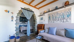 Uma sala de estar acolhedora com um arco de pedra que dá para um quarto, um sofá com almofadas azuis e uma parede com arte inspirada em peixes.