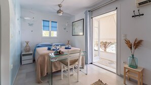 Quarto com cama, mesa de vidro, cadeira, janela, porta e vista para o exterior.