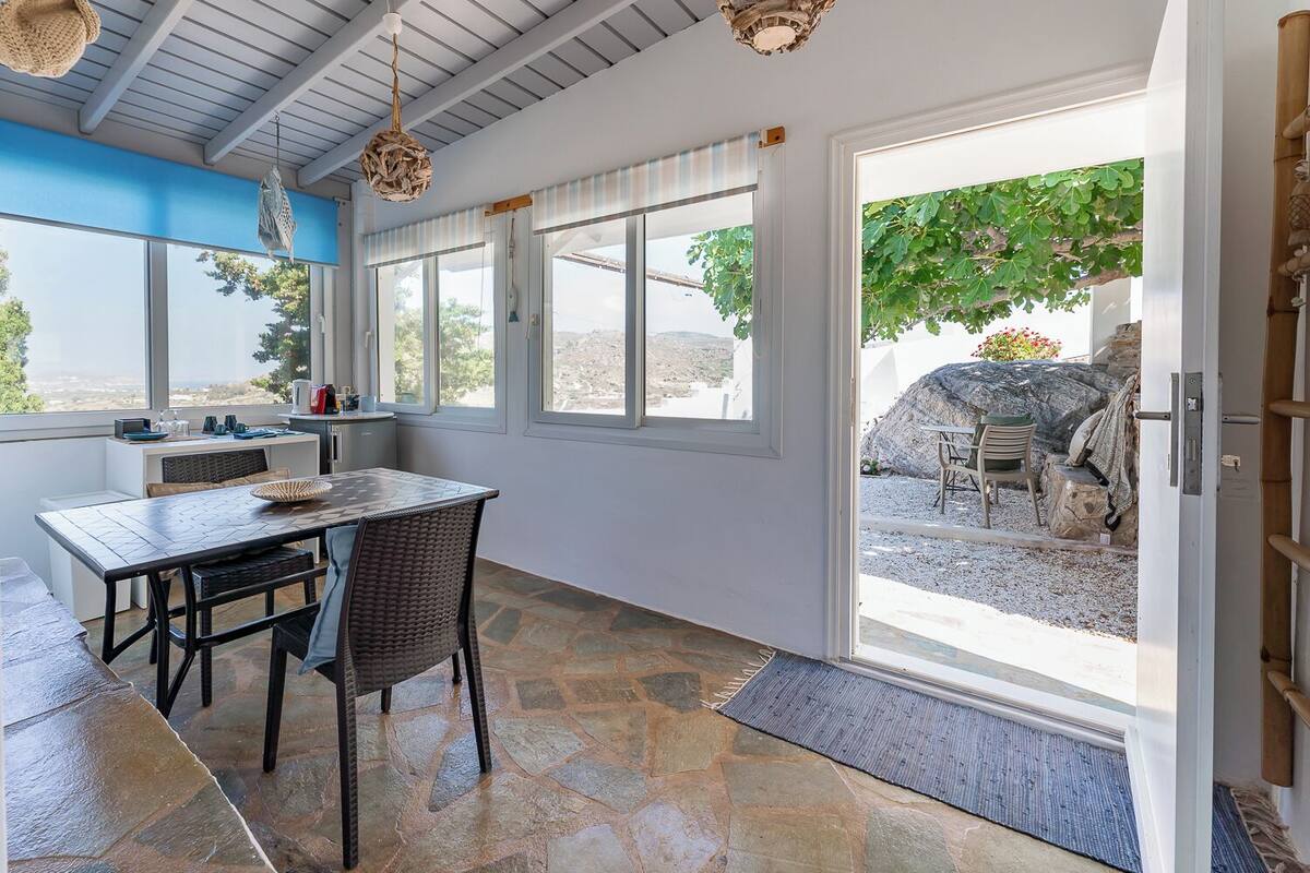 A dining area with a table and chairs, large windows, and a view of the outdoors.