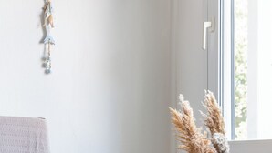 Quarto com uma cadeira de madeira, um travesseiro azul, um vaso branco e capim-do-campo.