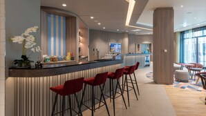 A modern bar area with a curved counter, red bar stools, and a decorative orchid plant. - Hampton by Hilton Munich City North (Munich)