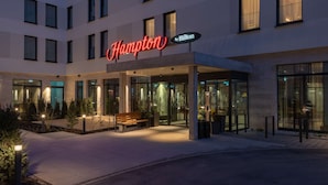 A modern hotel entrance with a prominent sign, outdoor seating, and a well-lit pathway. - Hampton by Hilton Munich City North (Munich)