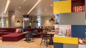 A modern library with a red sofa, wooden tables, and bookshelves. - Hampton by Hilton Munich City North (Munich)