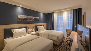 A hotel room with two beds, a desk, and a large window with curtains. - Hampton by Hilton Munich City North (Munich)