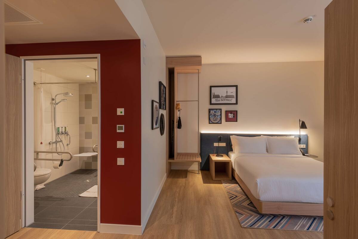 A modern hotel room with a shower, toilet, bedside table, and a bed.
