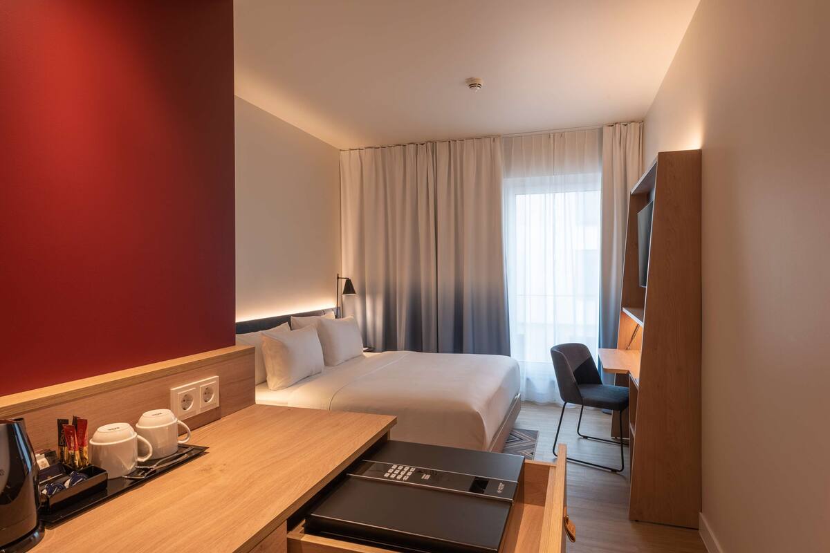 A hotel room with a bed, a desk with a coffee maker, a TV, and a chair.
