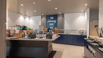Un'area colazione moderna con un bancone centrale, distributori automatici di bevande e diverse opzioni per la colazione.