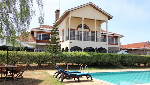 A large house with a swimming pool, a patio with lounge chairs, and a well-maintained garden. - Kusyombunguo Hotel Lukenya (Athi River)