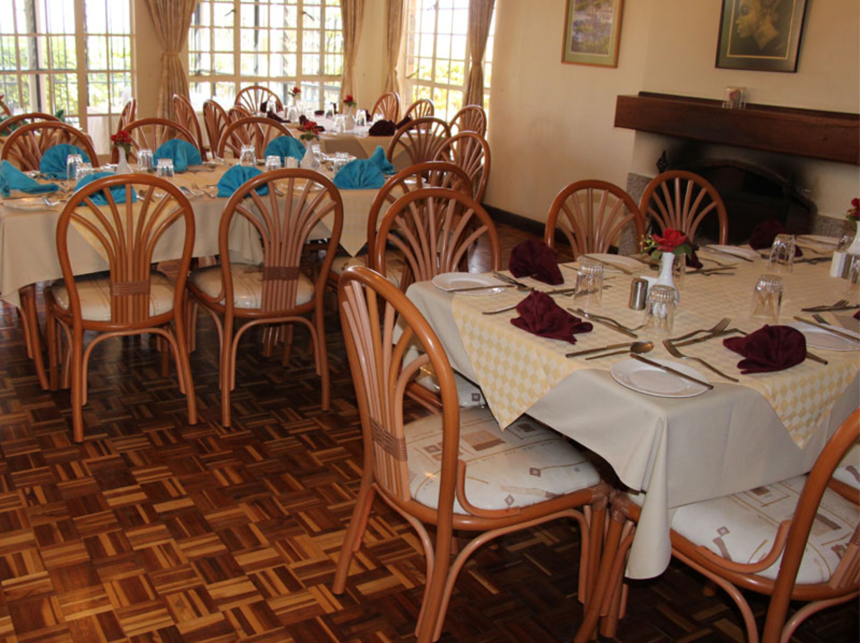 A dining area with wooden chairs and tables, each set with cutlery and napkins.