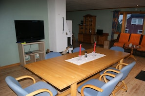 Un coin repas comprenant une table en bois, des chaises à revêtement bleu, un téléviseur et un meuble.