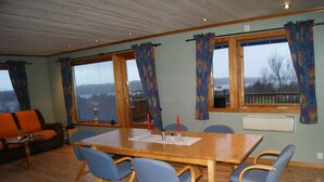 A dining area with a wooden table and blue chairs, a sofa, and large windows with curtains. - Vacation home on Bømlo perfect family vacation for hikers and cyclists (Rolvsnes)
