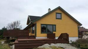 A yellow house with a green roof, a wooden deck, and a large window. - Vacation home on Bømlo perfect family vacation for hikers and cyclists (Rolvsnes)