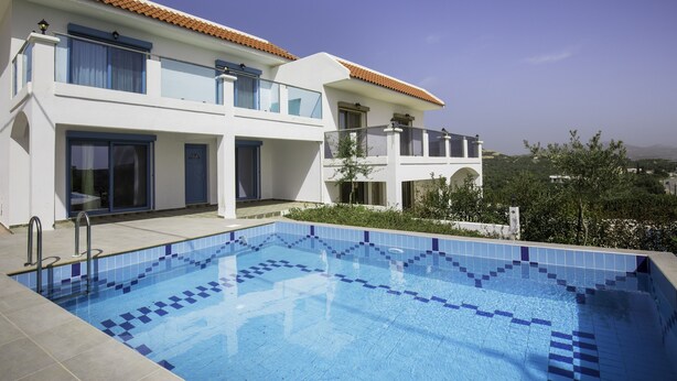 Una casa moderna de dos pisos con piscina, ventanas amplias y techo de tejas.