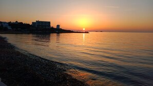 A sunset over a calm sea with buildings on the shore. - Semi-detached House on the Heights of Parikia - Exceptional View of the Cyclades (Paros)