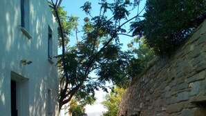 A narrow stone-paved alleyway flanked by white buildings and a stone wall, leading to a distant view. - Semi-detached House on the Heights of Parikia - Exceptional View of the Cyclades (Paros)