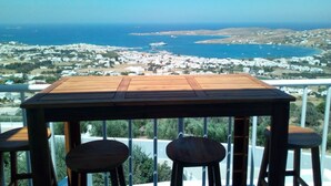 A wooden table with four stools, overlooking a coastal town with white buildings and a view of the sea. - Semi-detached House on the Heights of Parikia - Exceptional View of the Cyclades (Paros)