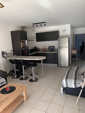 Een compacte keuken met een centraal eiland, een koelkast en een eethoek met barkrukken.