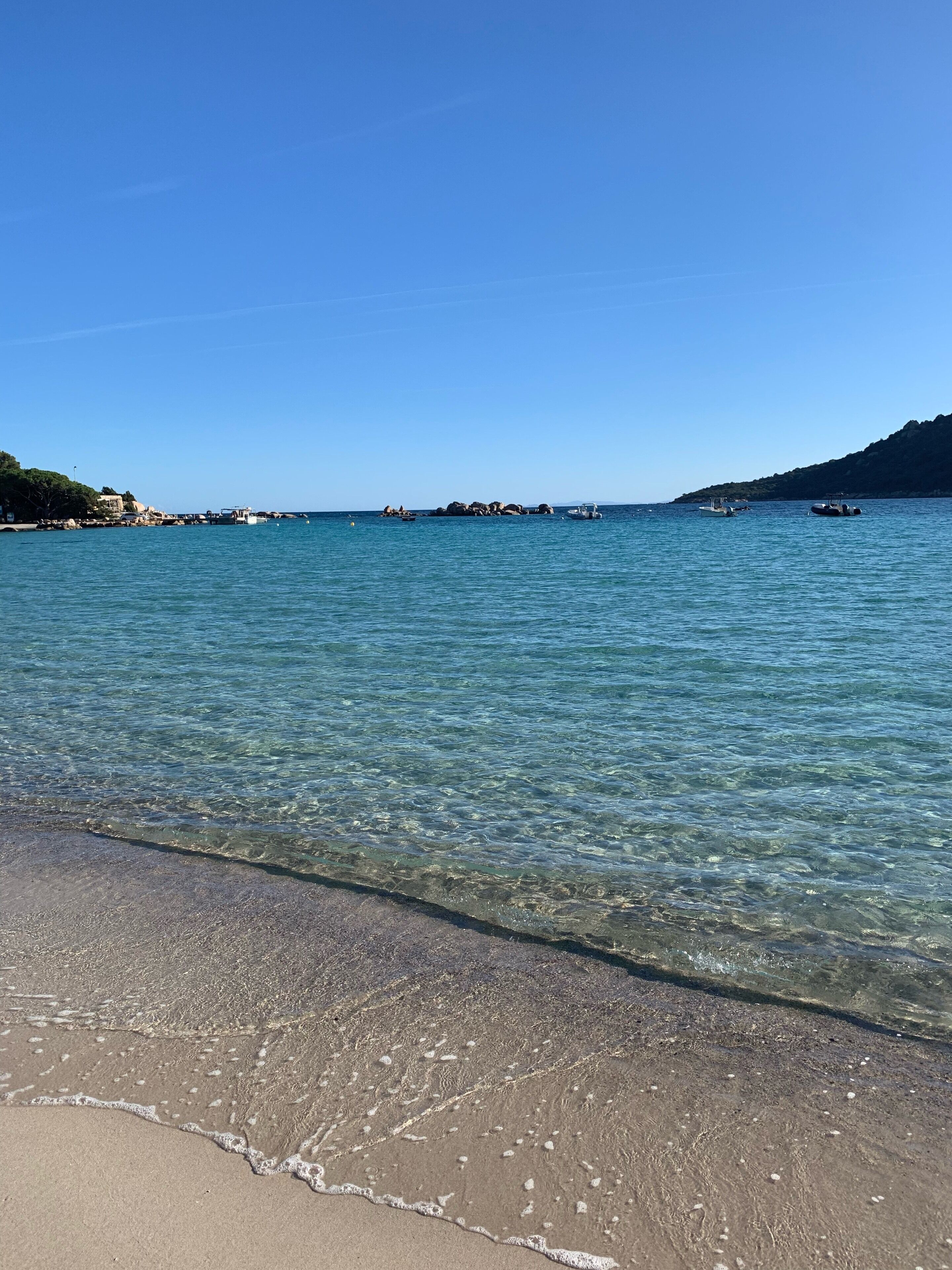 Een helder strand met rustig water en verafgelegen rotsachtige eilanden.