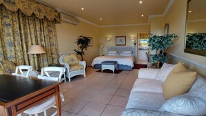 A hotel room with a bed, a sofa, a dining table, and chairs. There are potted plants and a mirror on the walls. - Roosboom Luxury Studio - With Sea View and Kitchen, Ideal for 2 Guests, Capetown (Cape Town)