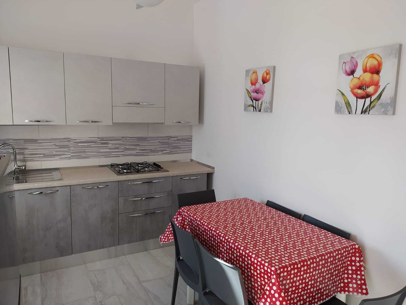 A kitchen with grey cabinets, a gas stove, and a red polka-dotted tablecloth-covered table.