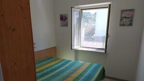 A small, single-bed room with a window, a door, and two wall-mounted pictures.