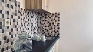 Una cocina con encimera negra, un armario de madera, un rebozo de azulejos y una lámpara colgante.