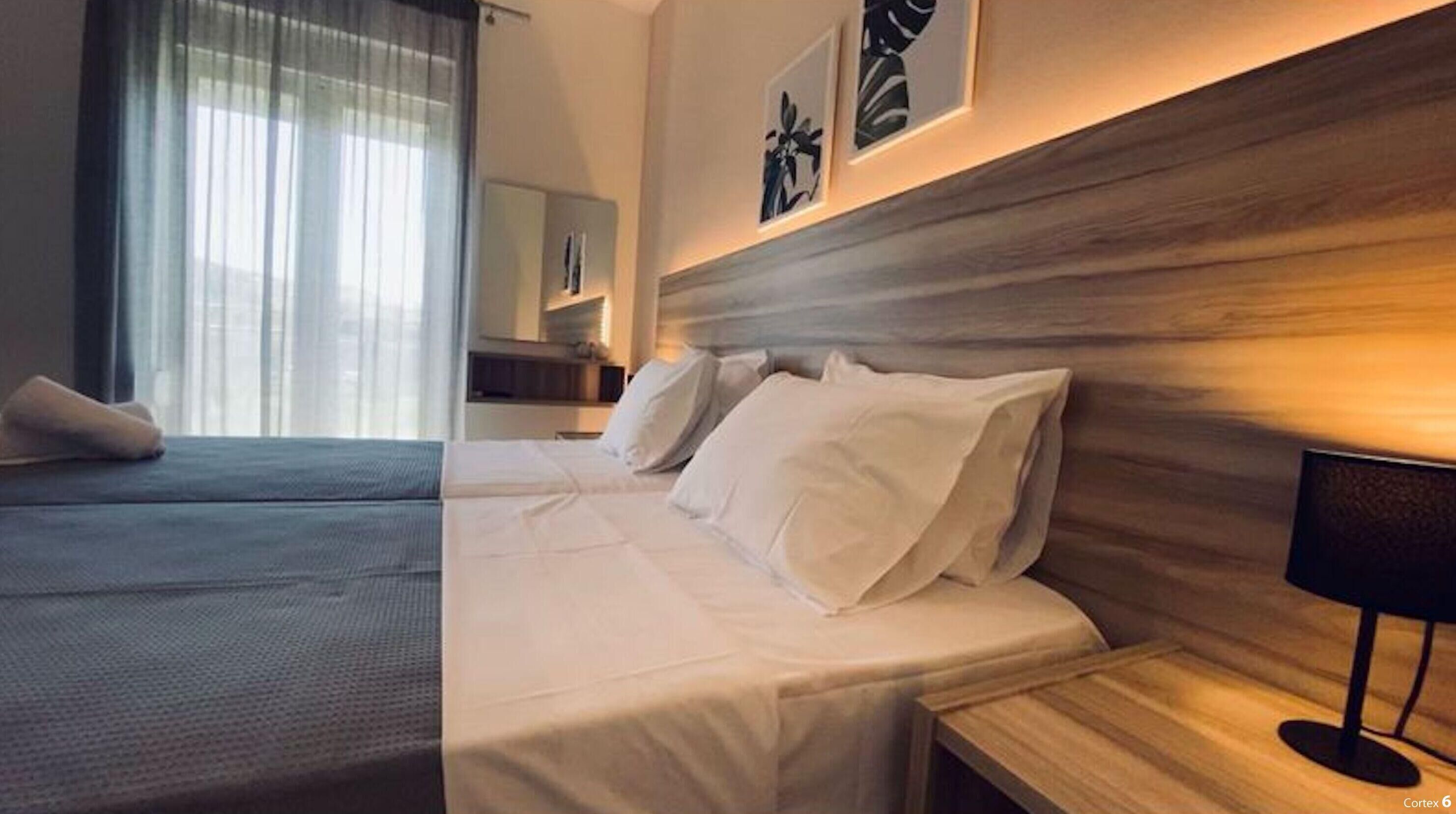 A hotel room with two beds, a wooden headboard, a nightstand with a lamp, and artwork on the wall.