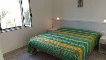 A bedroom with a bed, a window, a bedside table, and a wall-mounted light fixture.