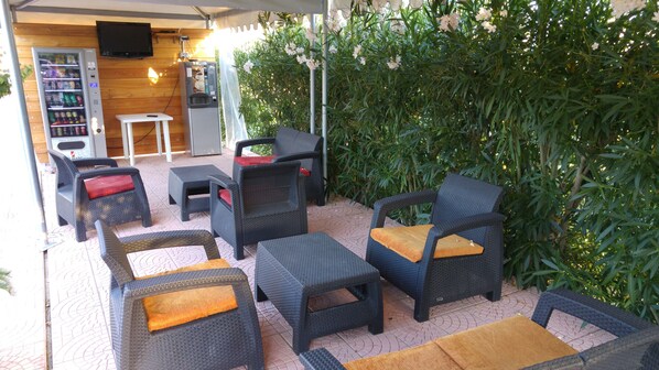 An outdoor seating area with wicker furniture, a beverage vending machine, and a television screen mounted on the wall.