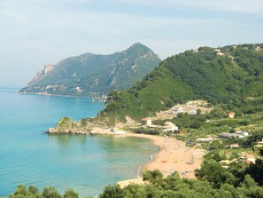 Enjoy a serene beachfront setting with views of the surrounding hills, featuring sun loungers and umbrellas.