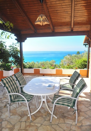 An outdoor patio with a round table and four chairs, overlooking a scenic view of the ocean.