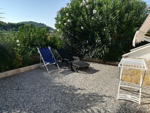 A patio with two lounge chairs, a small table, and a white shelf unit.