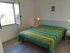 A bedroom with a bed, a window, a bedside table, and a wall-mounted light fixture. - Holidays in Vieste in Charming Villas - 5 (Vieste)