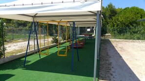 A playground with a covered area, green artificial turf, and a dirt path.