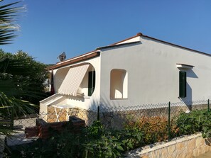 A white building with a red roof, a satellite dish, and a small window with green shutters.