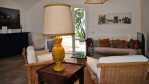 Un salon avec des meubles en osier, une lampe, un canapé avec des coussins et une étagère à plantes fixée au mur.