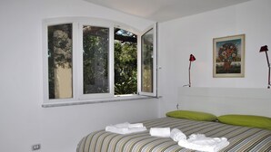 Une chambre à coucher avec un lit, des oreillers verts, une fenêtre donnant sur des arbres et un tableau accroché au mur.