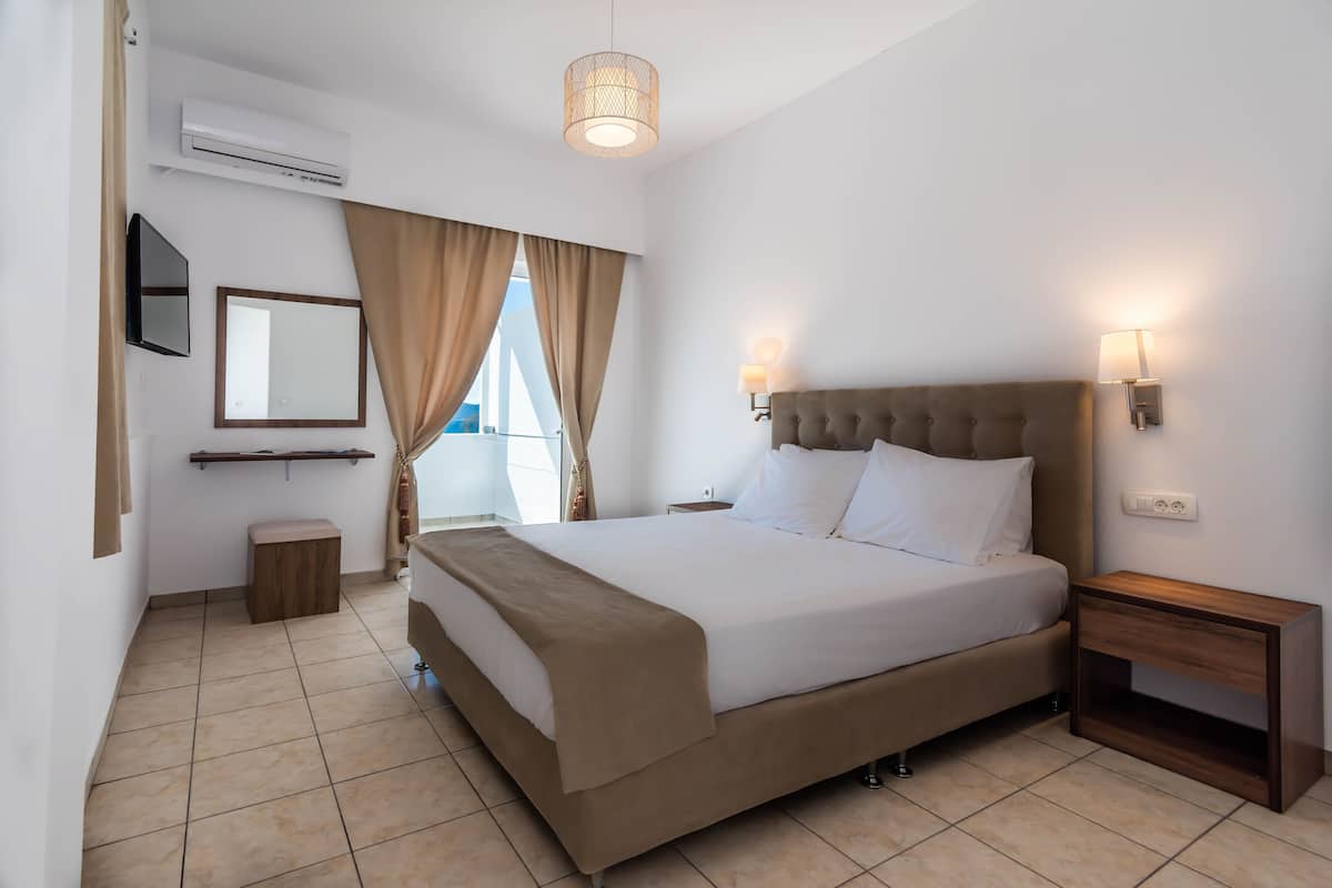 A hotel room with a large bed, a bedside table, a wall-mounted TV, and an air conditioning unit.