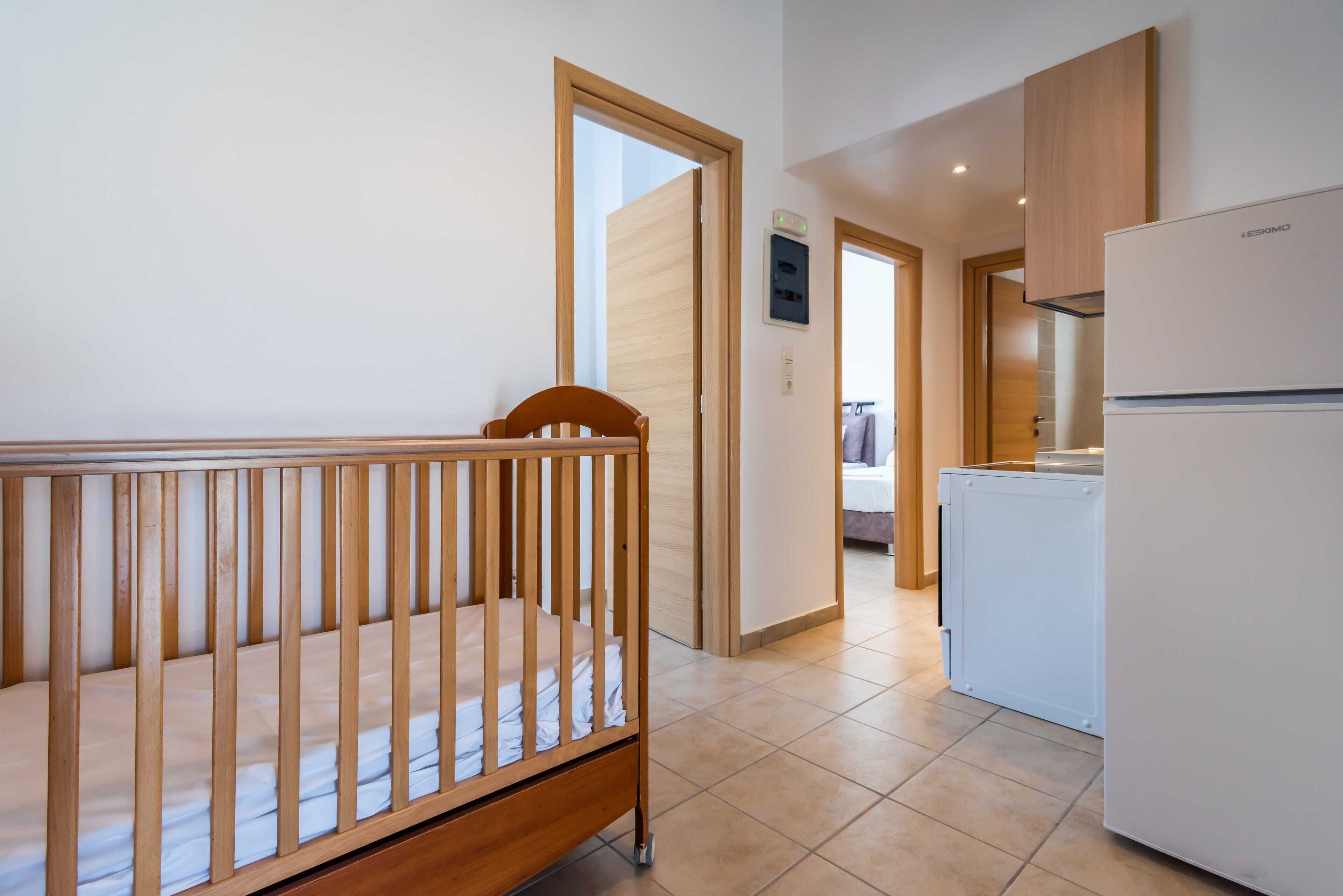 Ein Babybett in einem Zimmer mit Küchenzeile, inklusive Kühlschrank und Schränken.