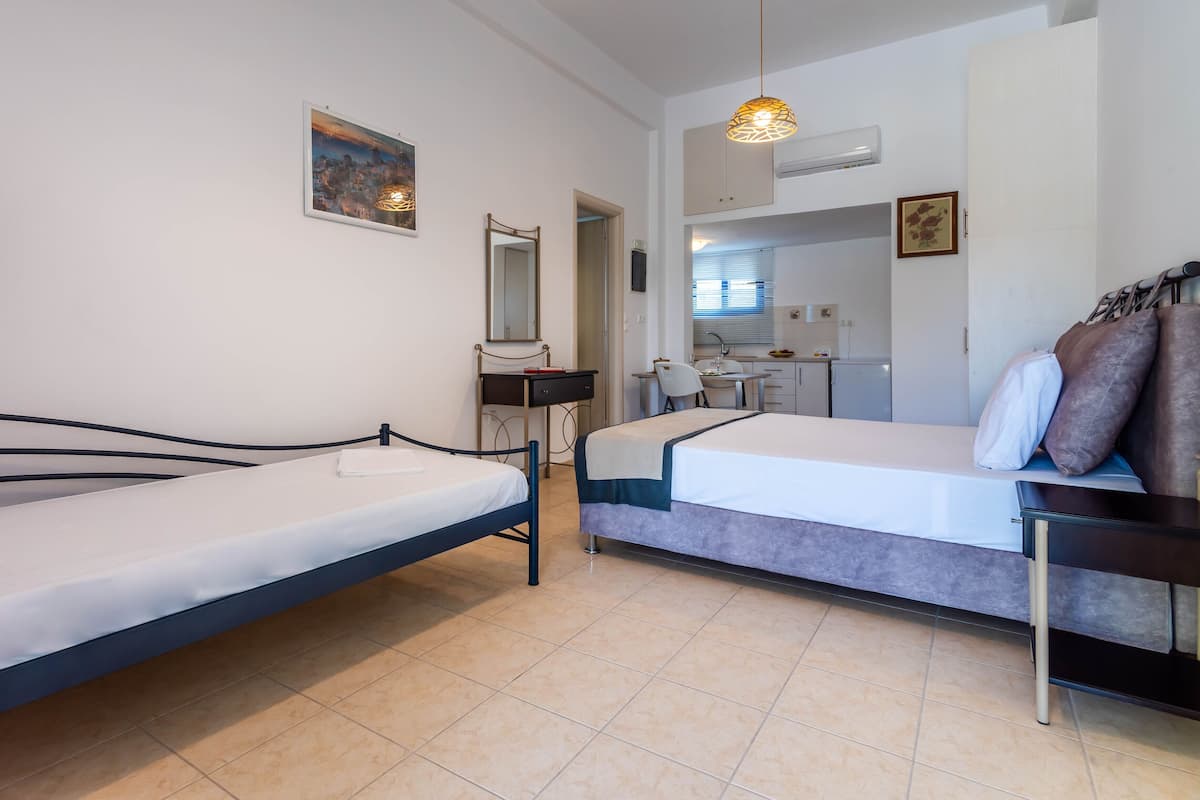 A room with two beds, a desk, a chair, a mirror, and a small kitchenette.