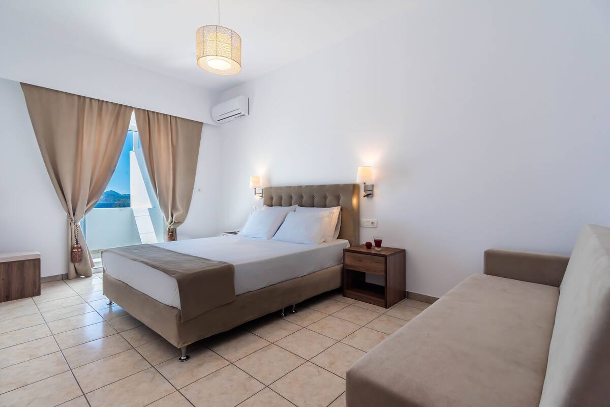 A hotel room with a bed, bedside table, and a view of the outdoors.