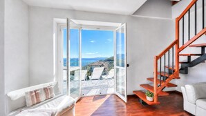 A modern interior with a wooden floor, a white sofa, a glass door leading to an outdoor area with a view, and a wooden staircase. - Penthouse The Magnifique View in Stresa (Stresa)