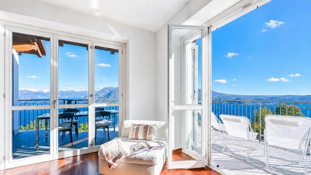 A spacious room with a large sliding glass door leading to an outdoor balcony with white chairs and a table. - Penthouse The Magnifique View in Stresa (Stresa)