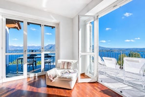 A spacious room with a large sliding glass door leading to an outdoor balcony with white chairs and a table.