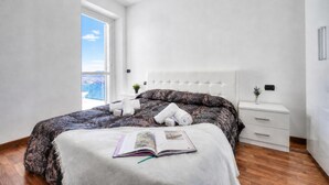 A bedroom with a large bed, a bedside table, a window with a view, and a door. - Penthouse The Magnifique View in Stresa (Stresa)