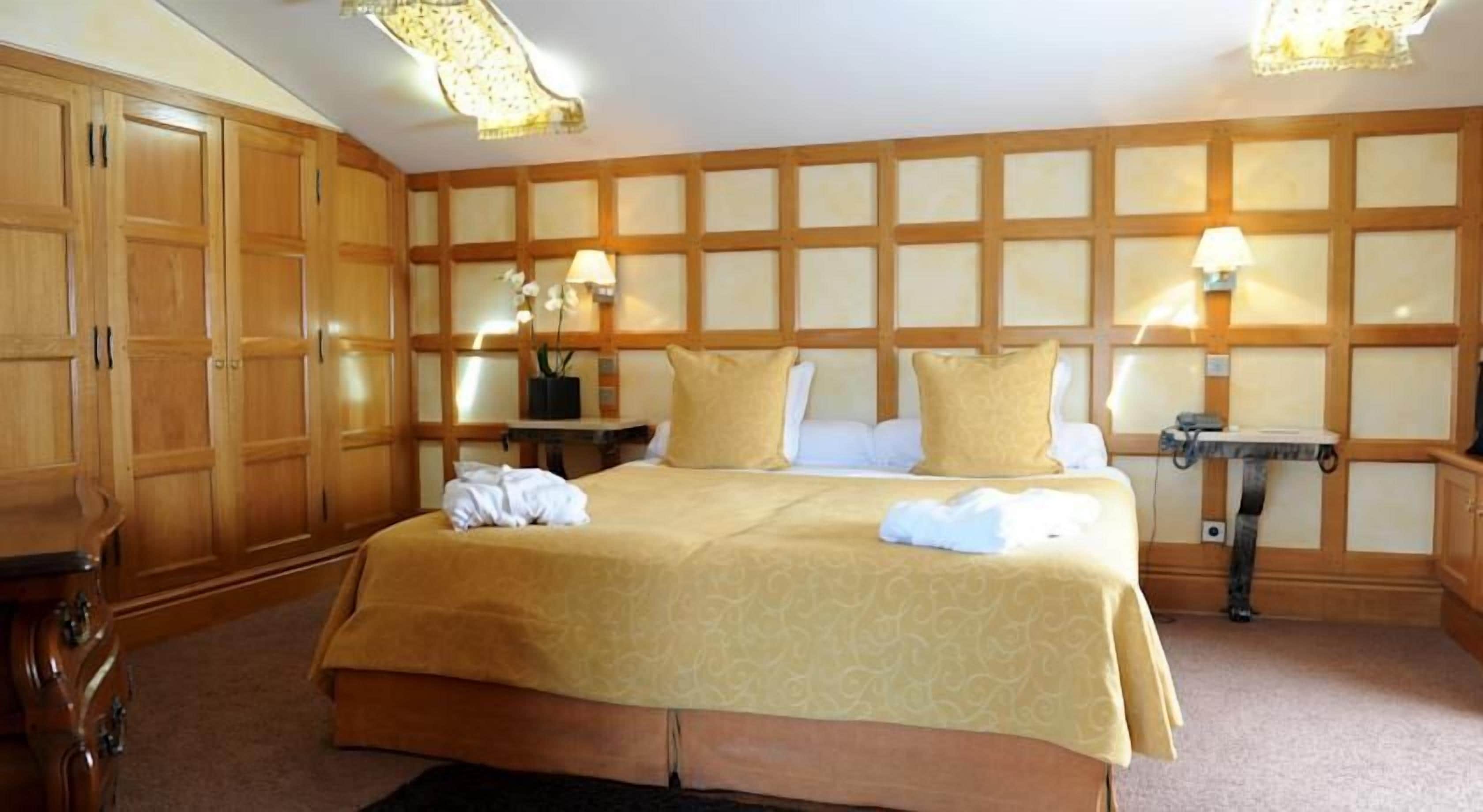 Habitación de hotel con una cama grande, un armario de madera, dos mesitas de noche con lámparas y suelo alfombrado.